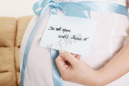 淡蓝色丝带摄影照片_怀孕的肚子上有一条淡蓝色的丝带和一个标签，上面写着“不要”