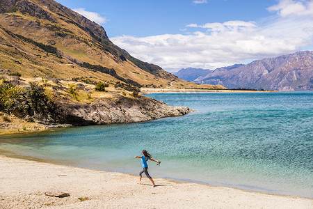 新西兰旅游快乐的旅游女性在哈威亚湖自然景观的海滩岸边享受快乐和自由。
