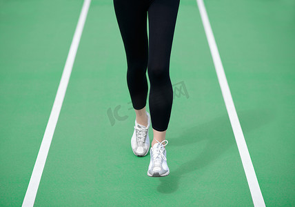 在公路上奔跑摄影照片_女运动员赛跑者脚在绿色跑道上奔跑。