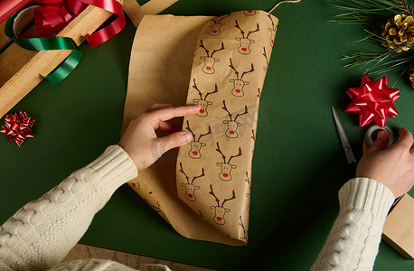 为圣诞节或新年活动包装礼物的顶级女性，使用带有鹿图案的漂亮装饰纸