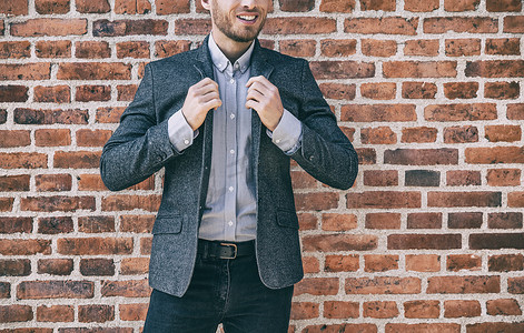 西装男士时尚休闲装年轻商人调整他蓝色羊毛西装外套的衣领与衬衫在办公室的砖墙背景下。