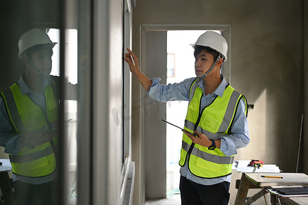土木工程师戴安全帽在建筑工地工作并在他的数字平板电脑上检查时间表的图像