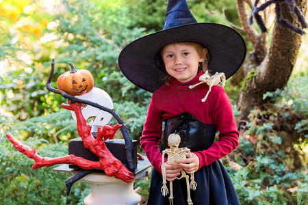 魔法师摄影照片_在万圣节派对上，穿着女巫服装的小女孩拿着一具骷髅