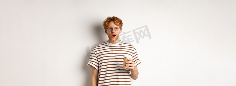 戴着眼镜的红头发男子拿着咖啡杯，完全不相信地盯着镜头，站在白色背景下的条纹 T 恤上