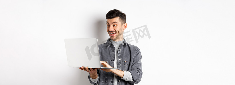 男人在笔记本电脑上看搞笑视频，对着电脑屏幕大笑，笑得开心，站在白色背景上