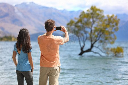 新西兰游客在湖边用手机拍摄瓦纳卡孤树。