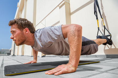 吊带摄影照片_健身男子在健身中心使用吊带做俯卧撑。