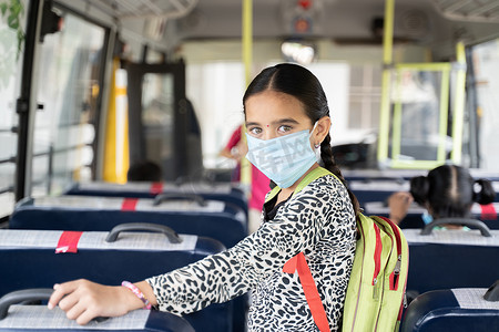 校车内戴医用口罩的女童画像看着相机 — 学校重新开放或以新的正常生活方式重返学校的概念