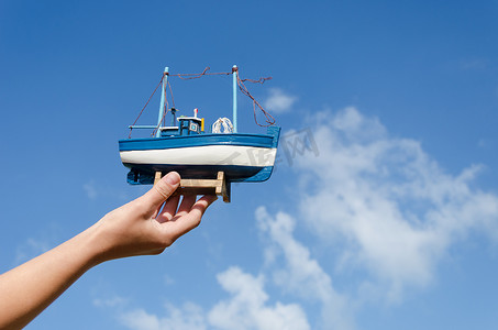 玩具帆船摄影照片_天空背景中的女性手持木船玩具