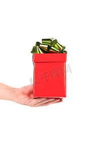 金色蝴蝶结摄影照片_手拿着带绿色金色蝴蝶结的红色盒子。