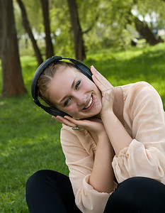 快乐的女人坐在草地上，在户外和 lau 听音乐