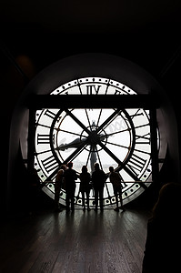 法国巴黎-2015 年 5 月 14 日：在奥赛博物馆里，身份不明的游客透过带有罗马数字的时钟的剪影。
