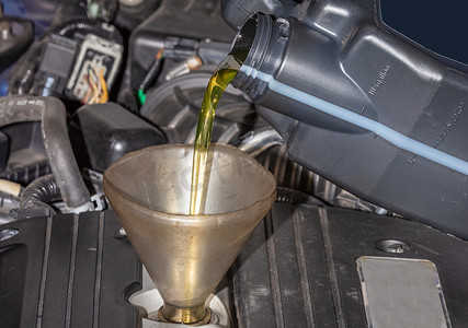 机械师在汽车中加满油，通过漏斗将一品脱油倒入发动机，关闭油和漏斗