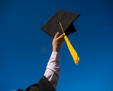 一个女人的手的特写镜头与蓝天的毕业帽。