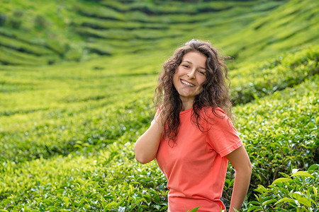 茶谷摄影照片_美丽的黑发女孩摆在绿茶灌木丛之间的茶谷中间。