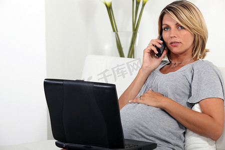 孕妇坐在沙发上，带着笔记本电脑和电话