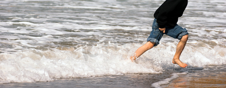 小男孩用脚奔跑在海洋海滩上冲浪崩溃的海泡沫