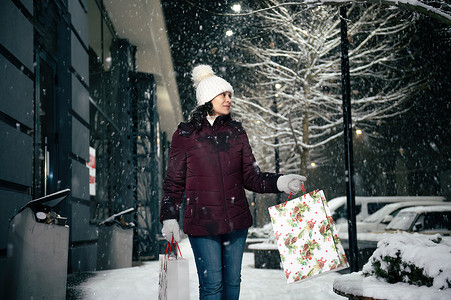 令人愉快的年轻女子走在街上，手里拿着购物袋，手里拿着圣诞礼品盒。