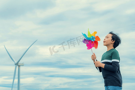 进步的年轻亚洲男孩在风力涡轮机农场玩风车玩具。