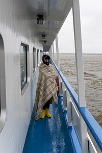 裹着格子呢的女人沿着海上航行的船的一侧行走