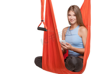 空中吊床摄影照片_坐在吊床上进行反重力空中瑜伽的年轻女子