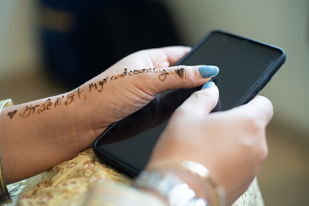 印度婚礼摄影照片_身着白金礼服准备婚礼的印度年轻女孩拿着手机，手机上写着“新娘将成为 BFF”，上面写着指甲花纹身