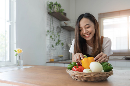 穿着围裙站在厨房里的年轻快乐女人的画像，准备用新鲜蔬菜和水果烹制健康食品。