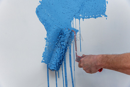在蓝色的男性手绘画墙壁与油漆滚筒。