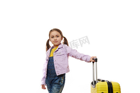 穿着紫色牛仔夹克的快乐小女孩，在白色背景上摆着黄色手提箱，上面有广告的复制空间
