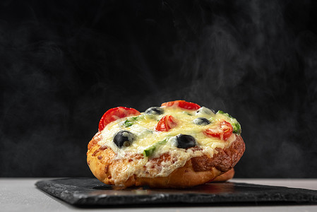 冒热气摄影照片_自制的热披萨在黑色背景上冒着热气。