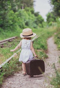 带铁轨的火车摄影照片_带着手提箱的迷人的婴孩沿铁路走