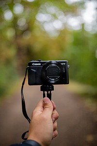 相机录像摄影照片_以模糊森林为背景的手持相机的肖像视图