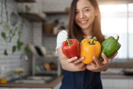 女孩备用摄影照片_穿着围裙站在厨房里的年轻快乐女人的画像，准备用新鲜蔬菜和水果烹制健康食品。