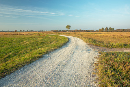 公路草地蓝天背景摄影照片_穿过草地和蓝天的乡村公路