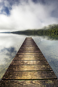 新西兰罗托鲁瓦的小船码头在平静的湖面上伸展，山上的薄雾升起
