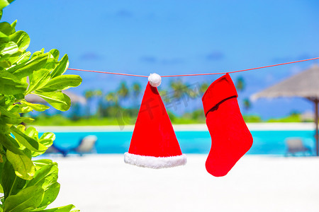 圣诞袜摄影照片_棕榈树间的红色圣诞帽和圣诞袜