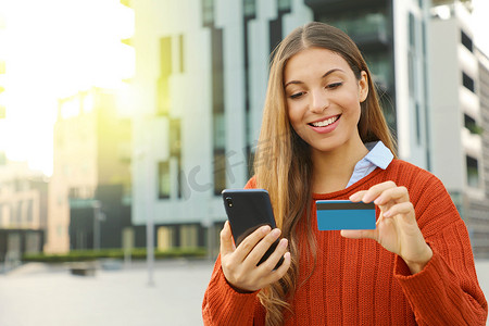 一个美丽幸福的女人的肖像输入信用卡号码，以便在户外用智能手机在线购买。