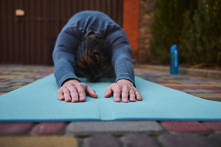 运动健身垫摄影照片_在瑜伽练习中伸展身体时，有选择地关注男性运动员或瑜伽士在健身垫上的手。