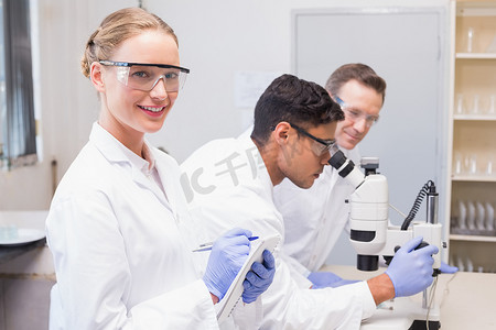 微笑的科学家看着相机，而同事们用显微镜工作