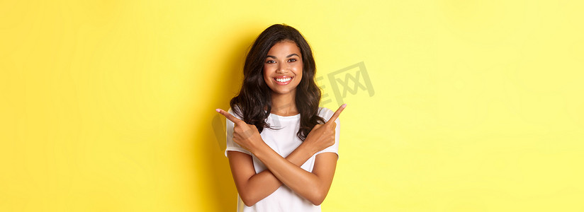 快乐而自信的非洲裔美国女孩的画像，展示了两种选择，手指横向指向左右复制空间，微笑着高兴，站在黄色背景上