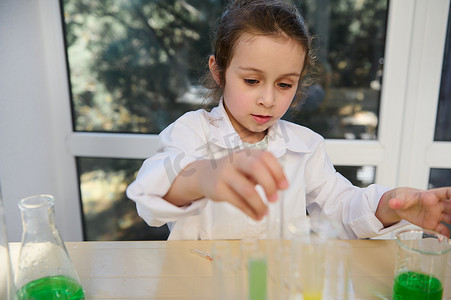 一个穿着白大褂的聪明可爱小女孩的特写，专注于学校化学实验室的化学实验
