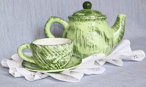 白色花边餐巾上的绿色茶壶和杯子