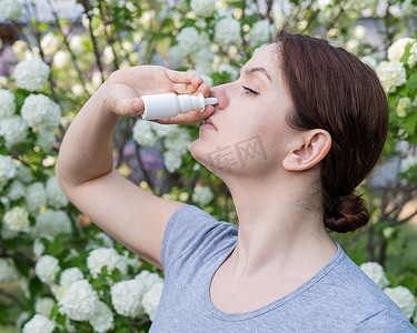 鼻腔喷雾剂摄影照片_白种女人在公园散步时使用喷鼻剂。