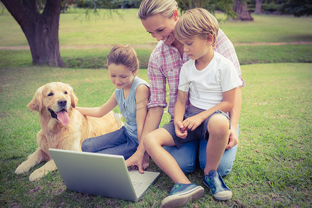 草坪和人摄影照片_幸福的家庭和他们的狗一起使用笔记本电脑
