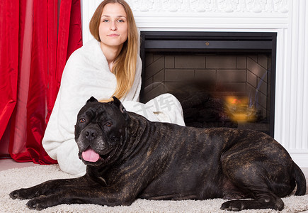 女孩和狗摄影照片_裹着毯子的女孩和狗 Cane Corso 坐在壁炉旁