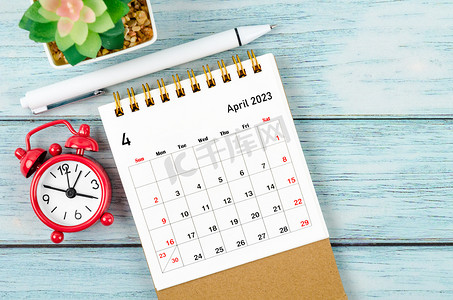 2023 年 4 月的月度台历，供组织者在木桌上计划 2023 年的闹钟和钢笔。