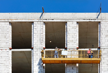 立起来打开的书摄影照片_建筑工人爬上正在建设中的建筑物立面上的支架。