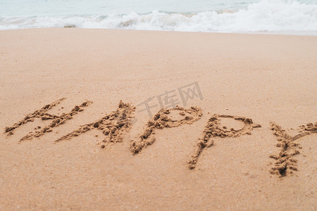 快乐的词手绘在沙滩上的夏日海滩上。