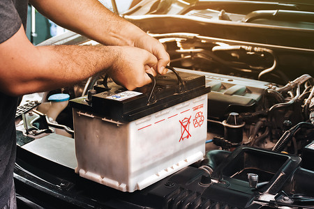 汽车知识摄影照片_汽车机械师携带用于汽车电气维护的更换汽车电池