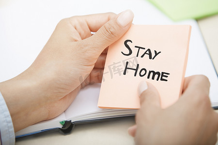 手拿着粉红色便条，上面写着“待在家里”的文字
